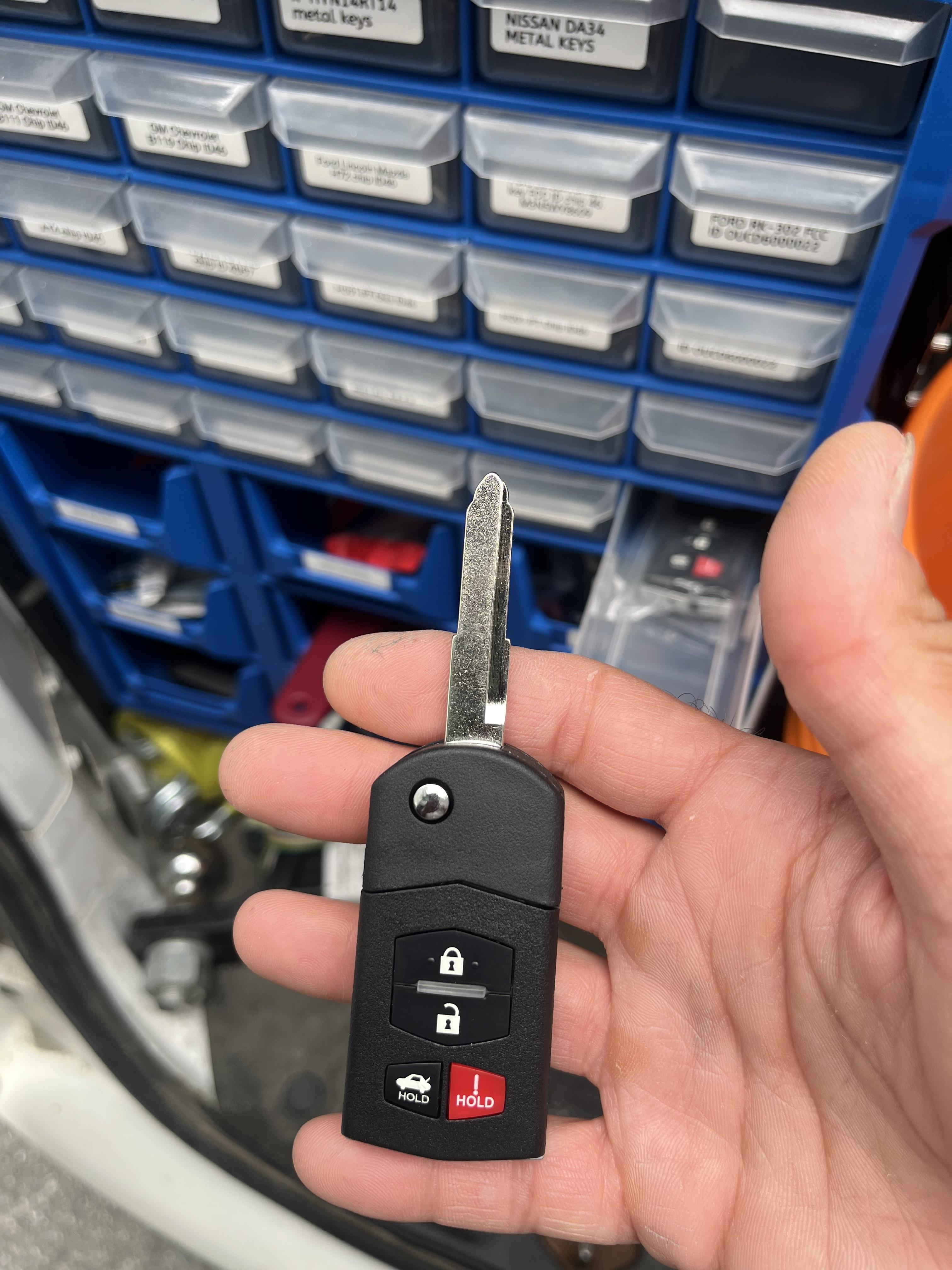 Replacement car key fob with uncut blade held in front of automotive key blanks