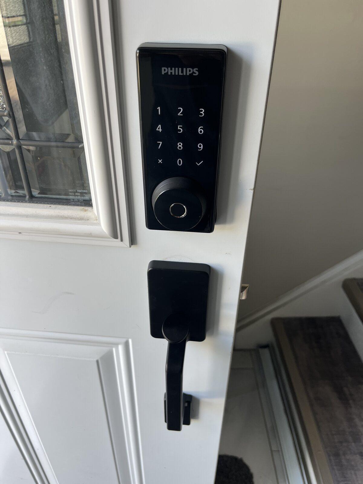 Black Philips fingerprint keypad deadbolt installed above a matching lever on a white residential entry door